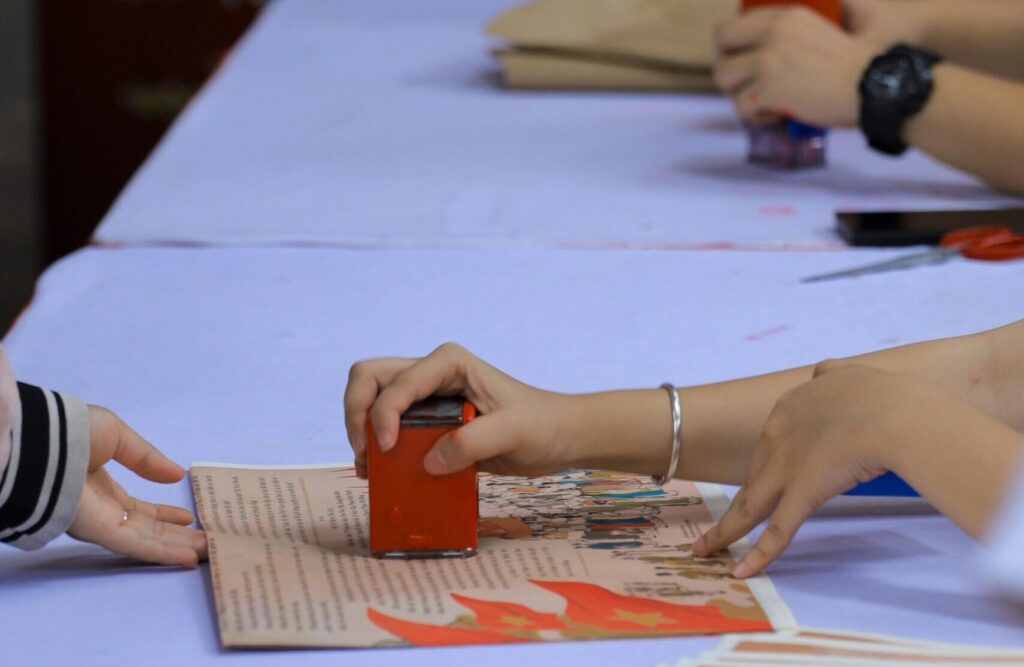 People hand-stamping red prints on paper sheets during a cultural event in Hanoi, Vietnam.